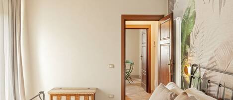 Un dormitorio con una cama, un banco de madera, una silla y una puerta que da a un baño.