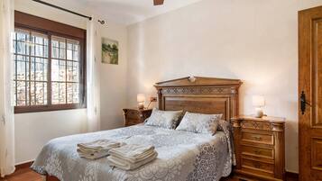 Un dormitorio con una cama grande, cabecera de madera, dos mesitas de noche con lámparas, una ventana con cortinas y un armario de madera.