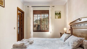 Une chambre à coucher avec un lit, une fenêtre avec des rideaux, une porte en bois et une table de chevet avec une lampe.