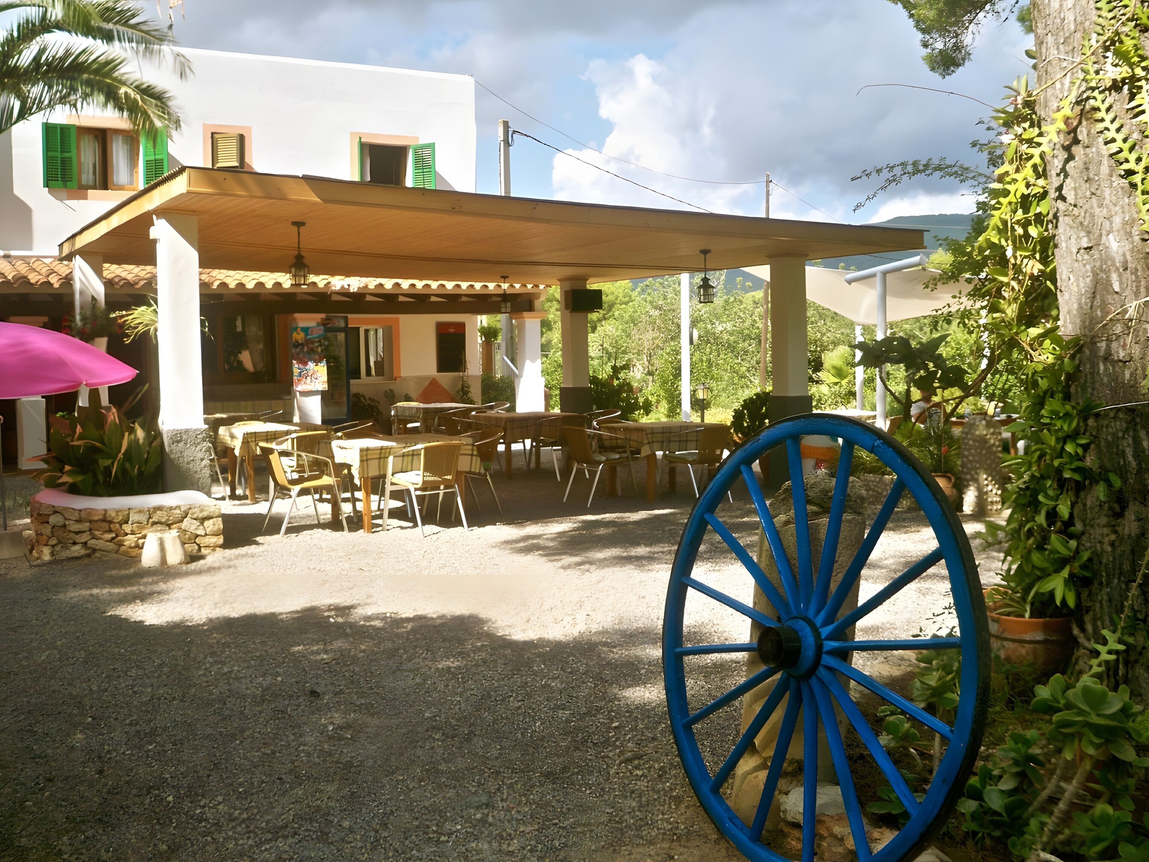 Un área de estar al aire libre con mesas y sillas, un porche cubierto y una rueda azul en primer plano.