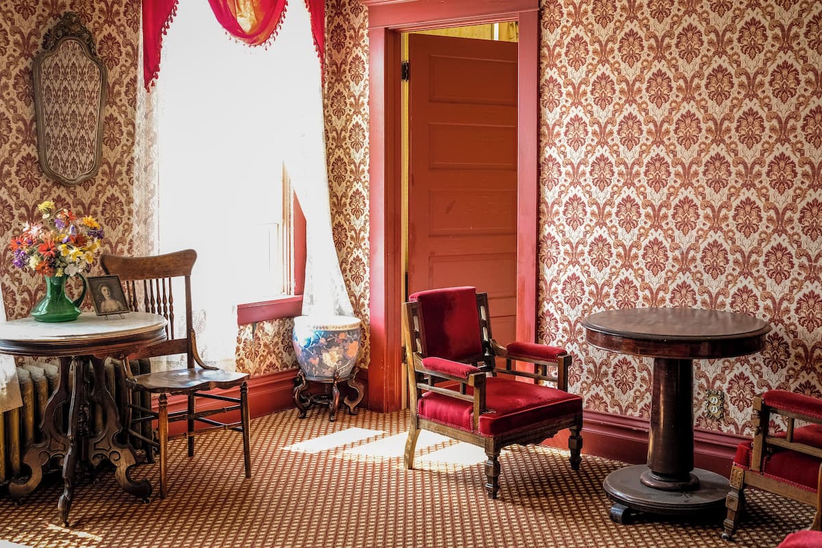 A room with patterned wallpaper, a red door, a round table, and a red chair.