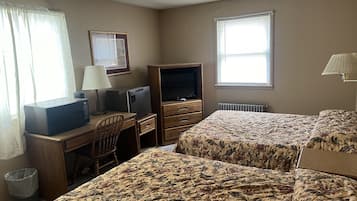 A hotel room with two beds, a desk with a television, a chair, a lamp, and a window with blinds.