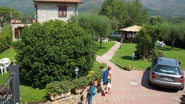 Un bâtiment en pierre, doté d’un toit en tuiles, entouré d’une végétation luxuriante et accessible par une allée pavée.
