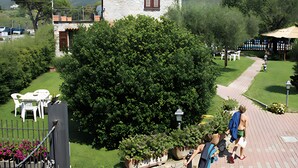 Un bâtiment en pierre doté d’un balcon, entouré d’une végétation luxuriante et bordé d’un chemin pavé.