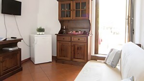 Ein Zimmer mit Bett, einer kleinen Küchenzeile, einem Fernseher und einem Fenster.