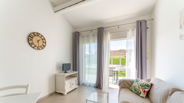 A living room with a sofa, a small table, a TV on a cabinet, and a clock on the wall. - Holiday Home 'Chez Céline' with Private Pool, Wi-Fi and Air Conditioning (Aubignan)