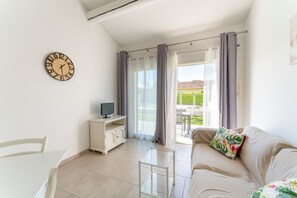 A living room with a sofa, a small table, a TV on a cabinet, and a clock on the wall. - Holiday Home 'Chez Céline' with Private Pool, Wi-Fi and Air Conditioning (Aubignan)