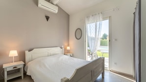 A bedroom with a bed, bedside tables, an air conditioner, a window with curtains, and a view of the outside. - Holiday Home 'Chez Céline' with Private Pool, Wi-Fi and Air Conditioning (Aubignan)