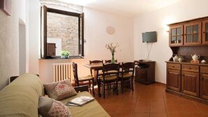 A living room with a sofa, a dining table with chairs, a kitchen area with cabinets, and a window with a view. - Apartment 'Ciclamino' with Shared Pool, Shared Garden and Wi-Fi (Campochiesa)