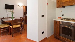 A kitchen with wooden cabinets, a stove, and a dining area with chairs and a table. - Apartment 'Ciclamino' with Shared Pool, Shared Garden and Wi-Fi (Campochiesa)