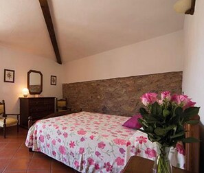 Ein Schlafzimmer mit Bett, Kommode, Spiegel und einer Vase mit Blumen.