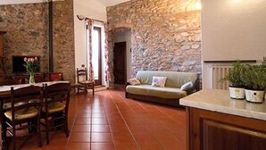 A stone wall, a wooden dining table with chairs, a sofa, and a television. - Apartment 'Dalia' with Shared Pool, Private Terrace and Wi-Fi (Campochiesa)