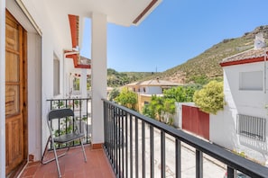 Een balkon met een stoel, een rood hek en uitzicht op een heuvel.