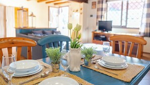 A dining table set with plates, glasses, and cutlery, surrounded by chairs, in a room with a wooden ceiling and a television in the background. - La Casa Di Gio - Dépendance in Villa (Viagrande)