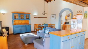 A cozy living room with a blue cabinet, a sofa, a dining table with chairs, and a kitchen area with a microwave. - La Casa Di Gio - Dépendance in Villa (Viagrande)