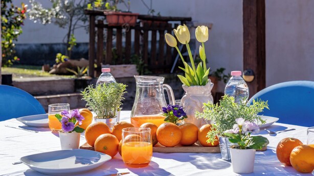 An outdoor dining area with a table set for breakfast, including plates, glasses, oranges, and a pitcher of orange juice. - La Casa Di Gio - Dépendance in Villa (Viagrande)