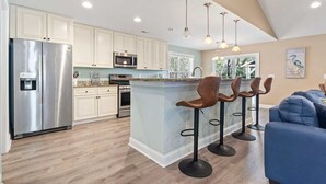 Una cocina moderna con una isla central, taburetes de bar, electrodomésticos de acero inoxidable e iluminación colgante.