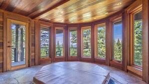 Une chambre dotée d’un grand lit, de murs en bois et de nombreuses fenêtres donnant sur des arbres et des montagnes.