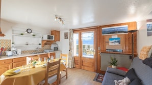 A cozy kitchen with wooden cabinets, a dining table set for two, and a view through a glass door to a snowy landscape.