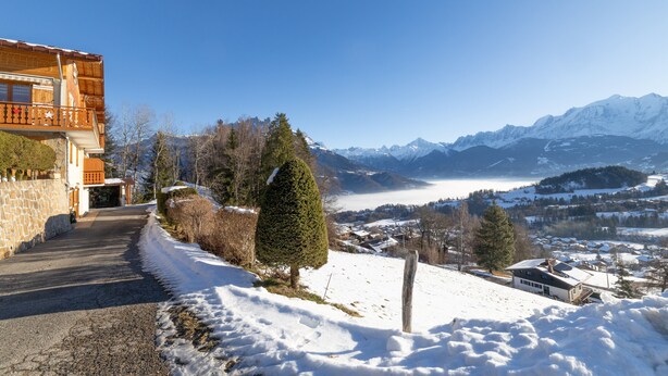 A mountain village with a wooden building, a snow-covered path, and a view of snow-capped mountains.