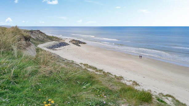 A beach with a clear view of the ocean, a sandy path, and some grassy areas.