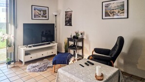 A living room with a television, a black leather chair, a table with a candle, and two remote controls.