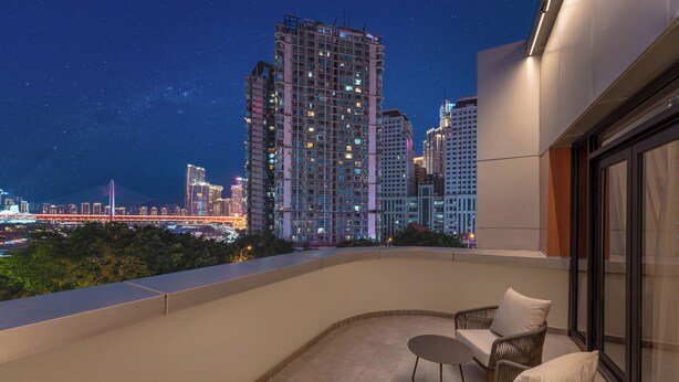 A balcony with wicker furniture and a view of a cityscape at night. - THE MUSTEL HOTEL CHONGQING. HONGYADONG (Chongqing)