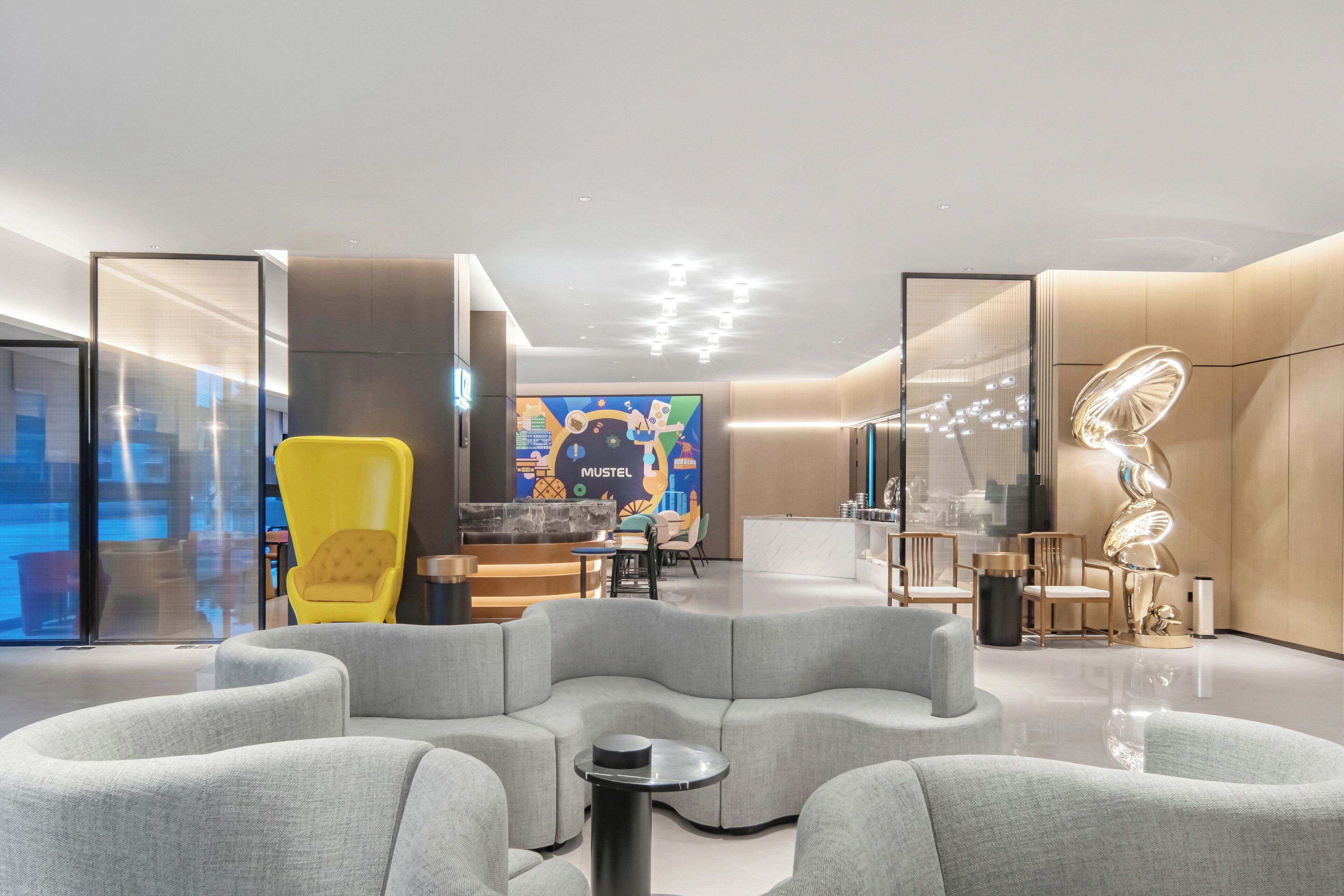 A modern lounge area with a curved grey sofa, a yellow chair, and a bar area in the background.