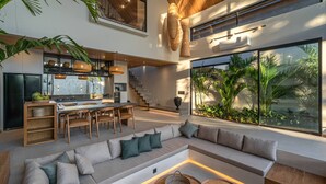A modern open-plan living area with a kitchen, dining space, and a large window overlooking a tropical garden. - Villa Bayu by GORO (Seminyak)