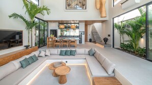 A spacious living area with a large sectional sofa, a dining table, and a kitchen in the background. - Villa Bayu by GORO (Seminyak)