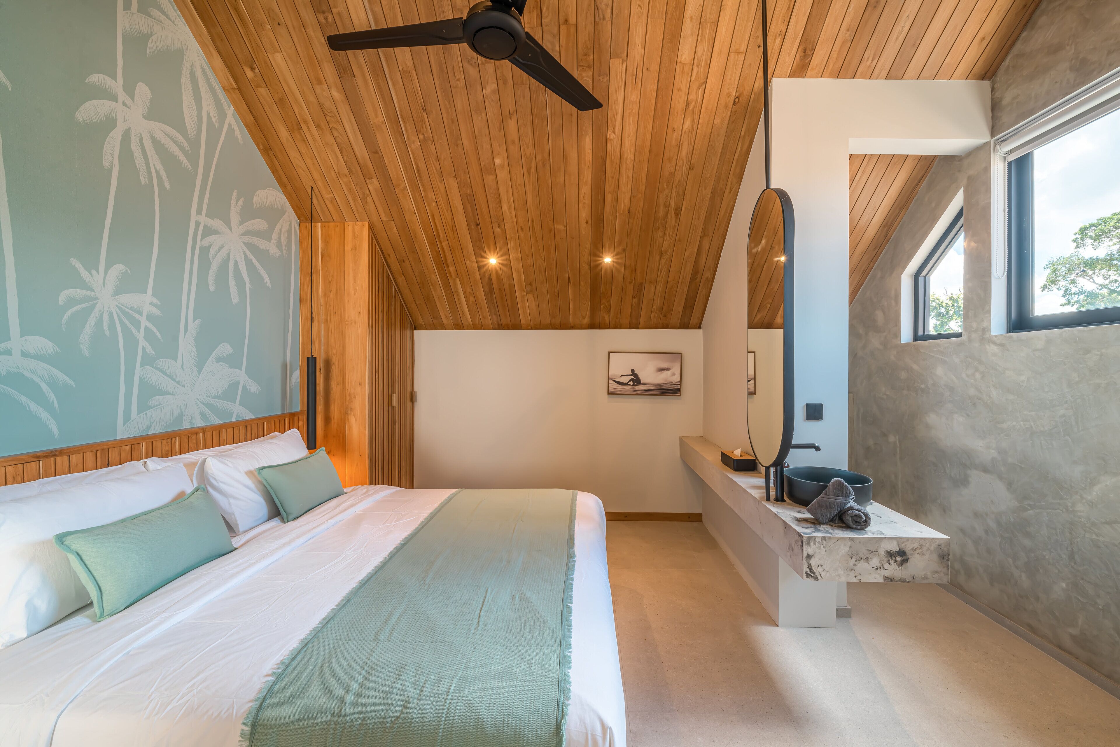 A modern bedroom with a wooden ceiling, a large bed, a built-in bench with a mirror, and a view of the outdoors.