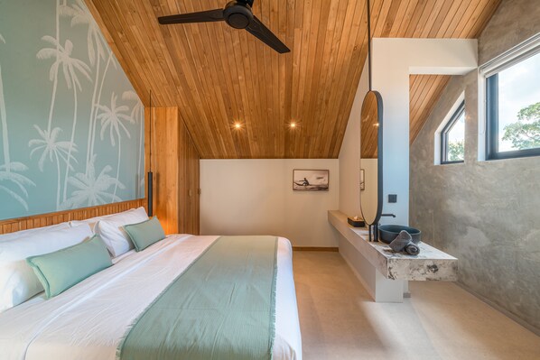 A modern bedroom with a wooden ceiling, a large bed, a built-in bench with a mirror, and a view of the outdoors.