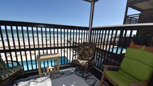 A balcony with a view of the beach, a pool, and a wooden chair. - Sea Oaks 103 - Oceanfront Complex in Garden City Beach (Garden City Beach)