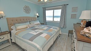 A bedroom with a large bed, a dresser, a nightstand, and a window with curtains. - Sea Oaks 103 - Oceanfront Complex in Garden City Beach (Garden City Beach)