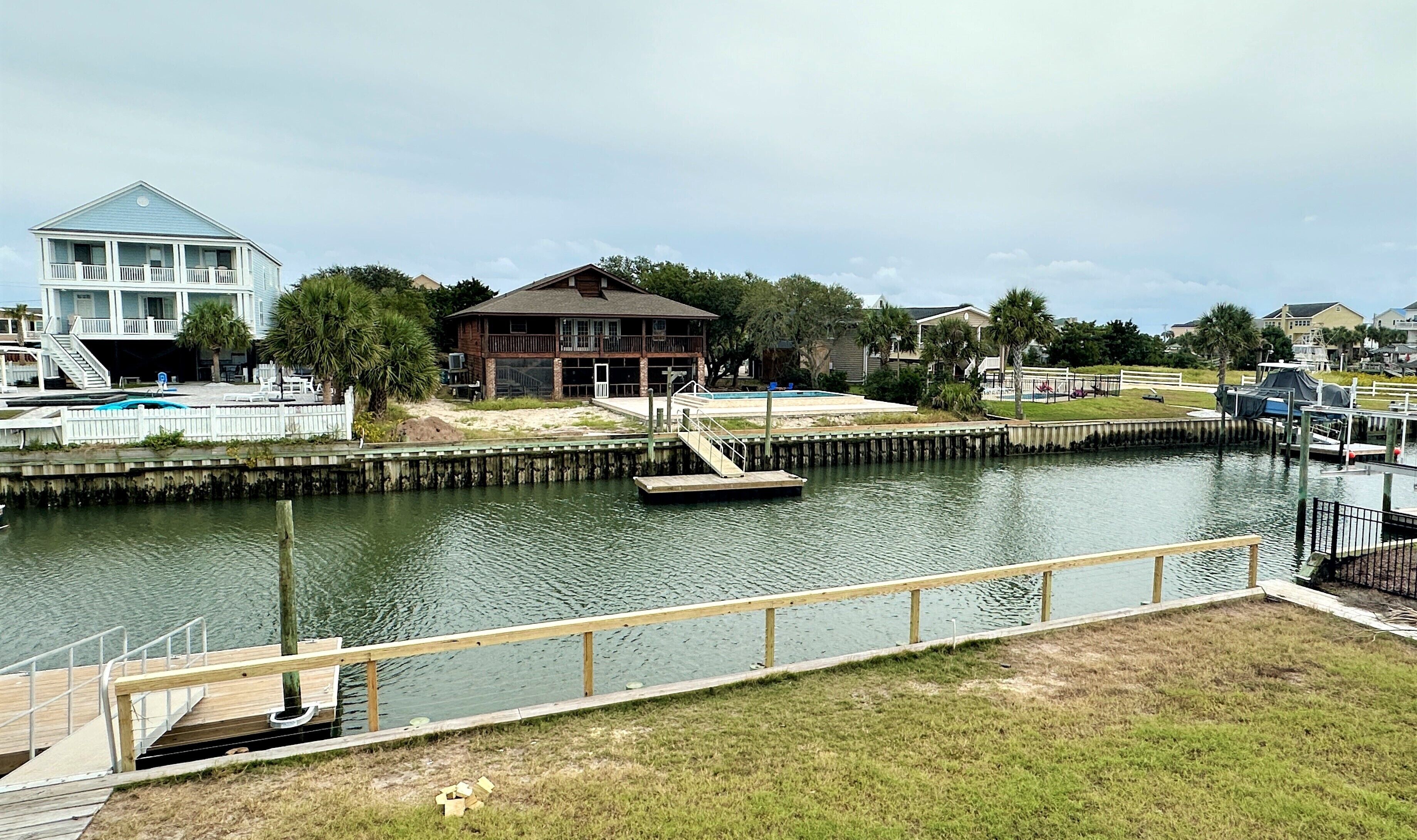 A waterfront property with a dock, a swimming pool, and a house with a balcony.