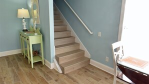 Un escalier menant à un deuxième étage, un plancher en bois, un mur bleu clair et une petite table avec une lampe.