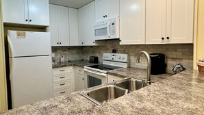 A kitchen with white cabinets, a stainless steel sink, a microwave, a stove, and a refrigerator. - Sea Oaks 102 - Oceanfront Complex in Garden City Beach (Garden City Beach)