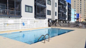 A swimming pool with a metal ladder, surrounded by multi-story buildings with balconies and windows. - Sea Oaks 102 - Oceanfront Complex in Garden City Beach (Garden City Beach)