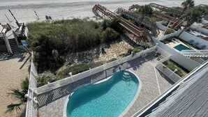 Un área de piscina con una piscina azul cristalina, terraza de madera y vista a la playa.
