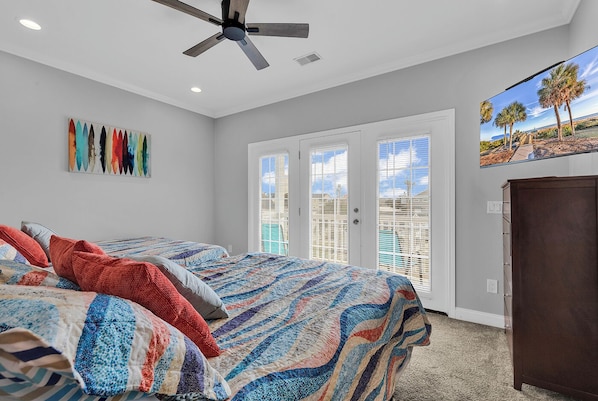 A bedroom with a bed, a ceiling fan, a door with a view, and a painting on the wall.