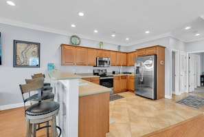 A modern kitchen with wooden cabinets, stainless steel appliances, and a bar area with stools.