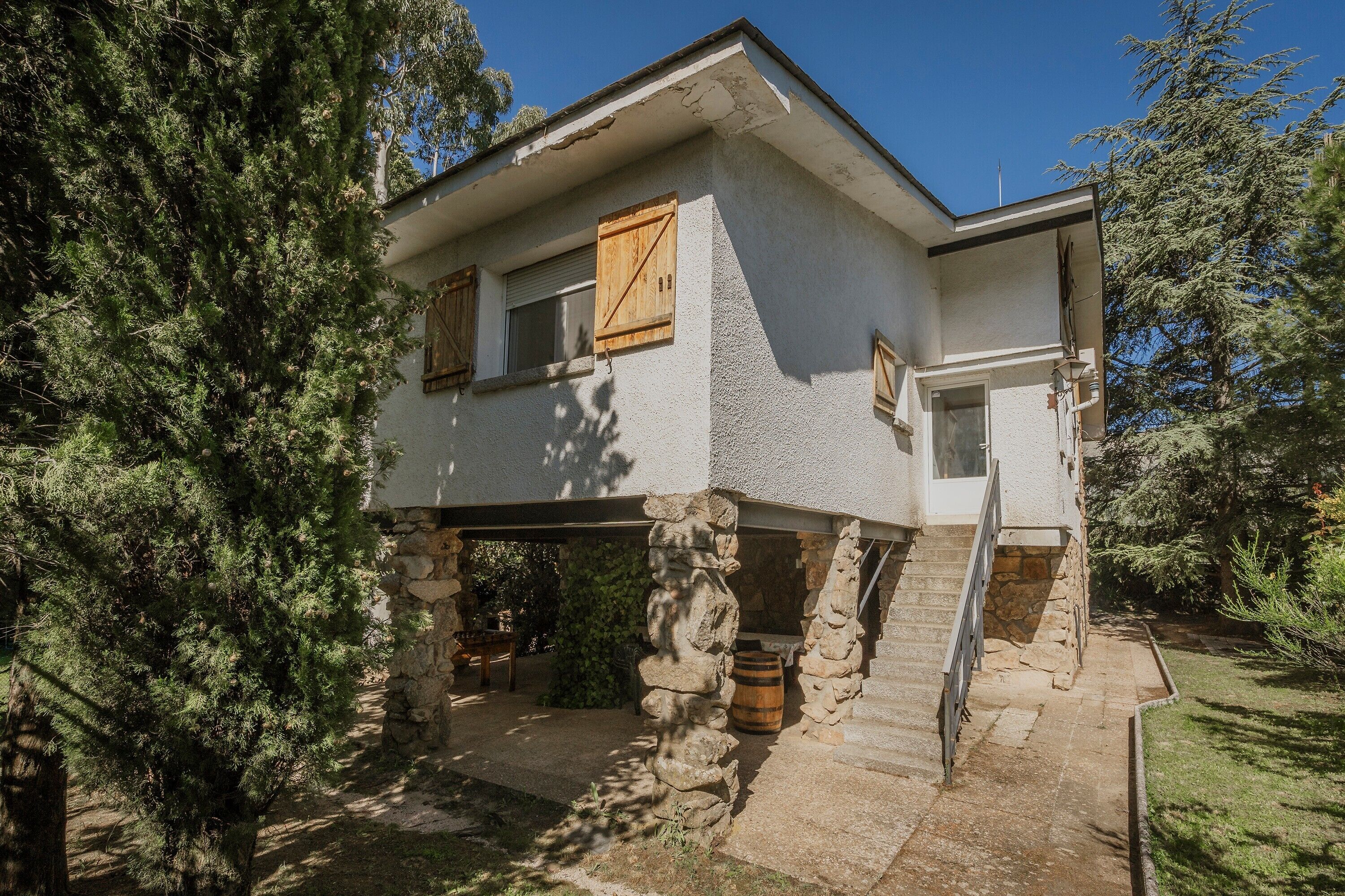 Una casa a due piani con fondamenta in pietra, persiane di legno e una scala in pietra che conduce all'ingresso.