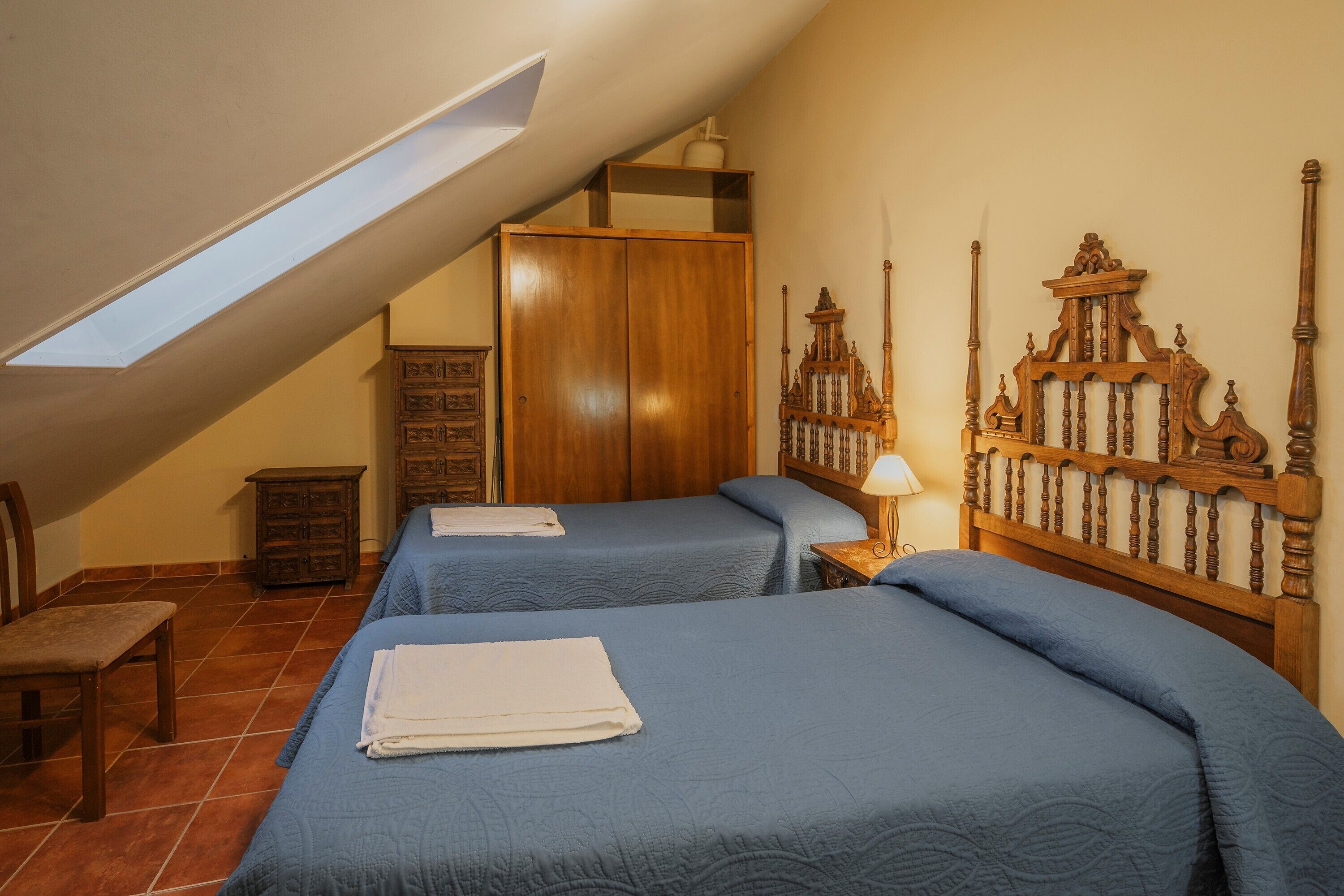 Une chambre avec deux lits, une armoire en bois, un petit meuble et une lucarne.