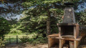Estructura de ladrillo al aire libre con horno y chimenea, rodeada de árboles y una zona vallada.
