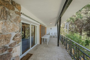 Un balcone con pareti in pietra, un tavolo, sedie e una ringhiera affacciata su un giardino.