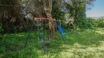 A playground with swings and a slide, surrounded by trees and grass.