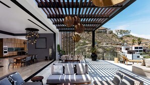 A modern outdoor living space with a dining area, seating, and a view of a hillside. - Brand-New Villa with Full Staff, 2 Pools, & Close to Downtown Cabo (Cabo San Lucas)