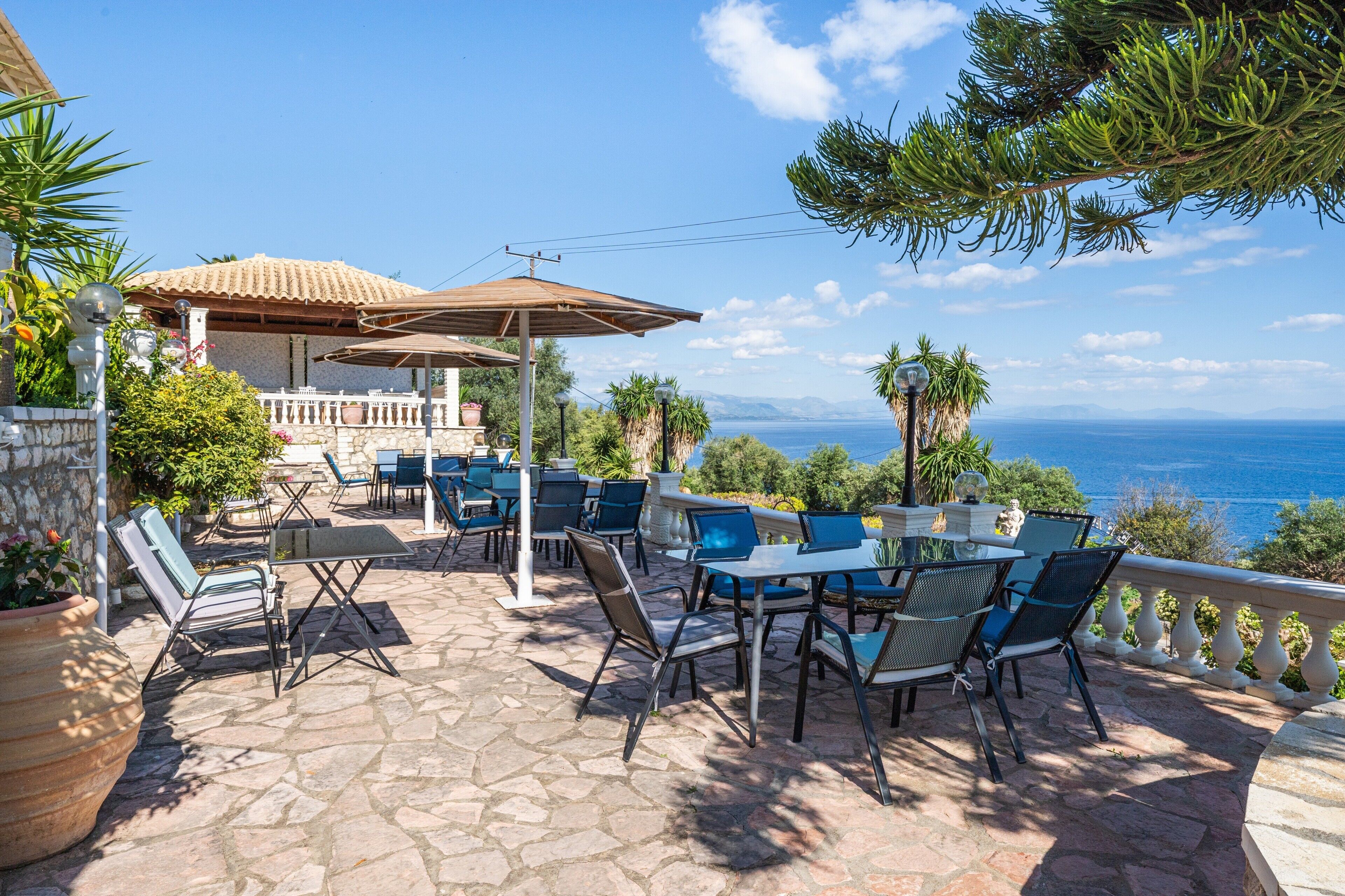 An outdoor patio with stone flooring, tables, chairs, and umbrellas.