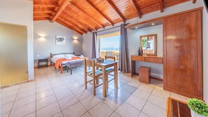 A room with a wooden ceiling, a bed, a desk, a chair, a window with curtains, and a small table.