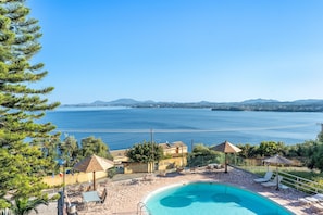 Ein Pool mit Liegestühlen, ein Gebäude mit einem Schild und Blick auf das Meer und die Berge.